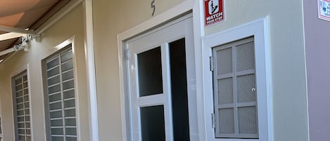 A building entrance with a white door, a security camera, and a 'Cuidado Con El Escalón' sign.