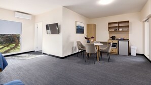 A modern hotel room with a large window, a flat-screen TV, a dining area with a table and chairs, a kitchenette, and a small refrigerator. - Inala Hotel (Inala)