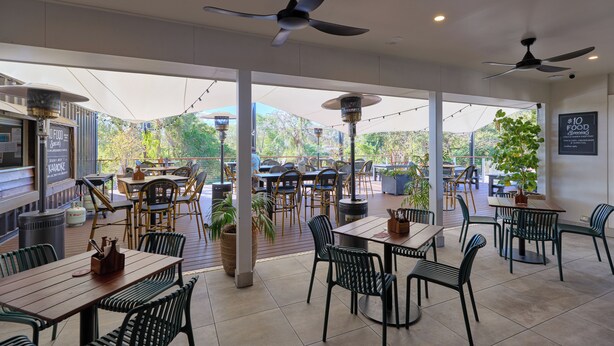 An outdoor dining area with tables and chairs, ceiling fans, and potted plants. - Inala Hotel (Inala)