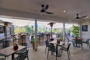 An outdoor dining area with tables and chairs, ceiling fans, and potted plants. - Inala Hotel (Inala)