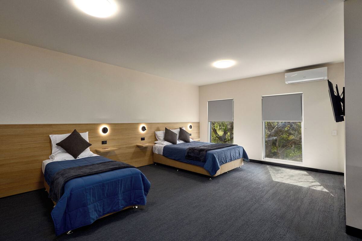 A modern hotel room with two beds, a large window, and a built-in air conditioning unit.