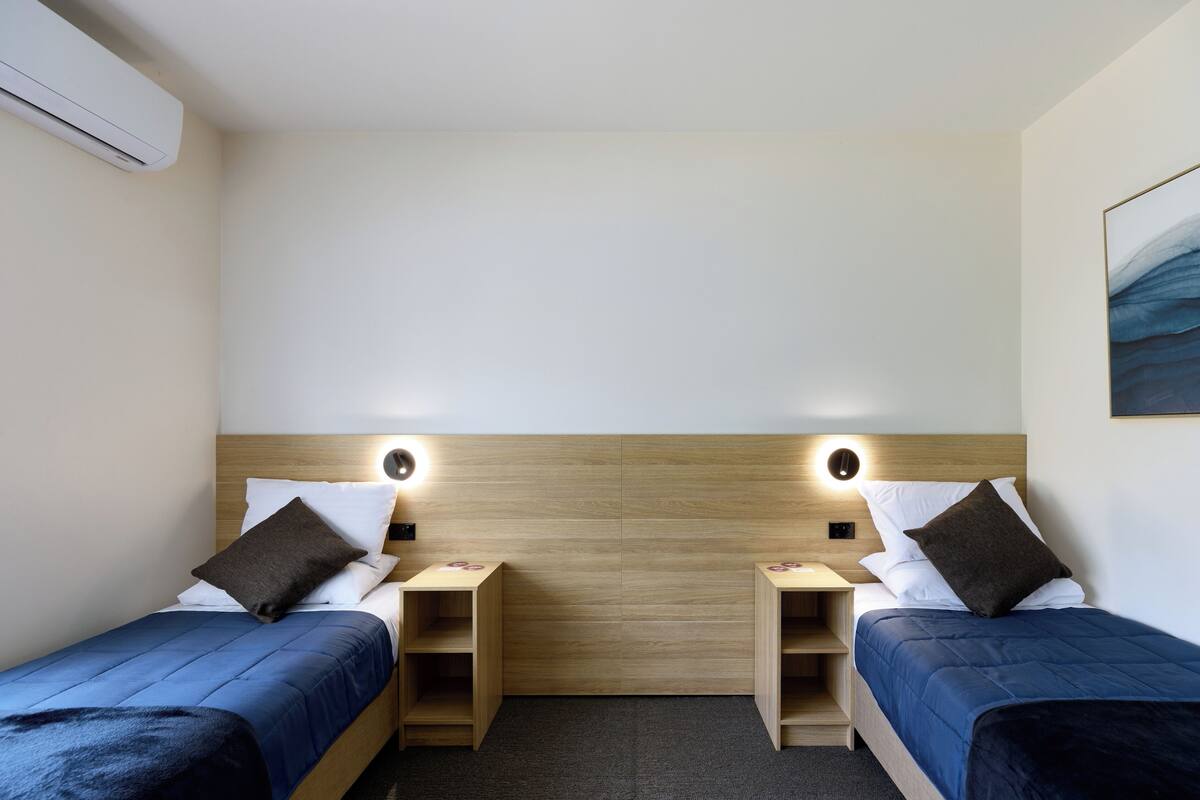 A hotel room with two single beds, each with a wooden headboard, a bedside table, and a nightstand.