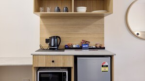 A kitchenette with a microwave, coffee maker, and a small refrigerator. There are shelves above the counter holding cups and a bowl. - Inala Hotel (Inala)