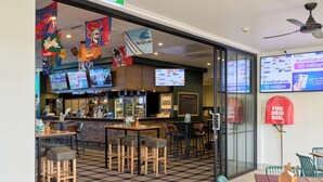 A restaurant with a bar area, multiple screens displaying sports, and a check-in counter. - Inala Hotel (Inala)
