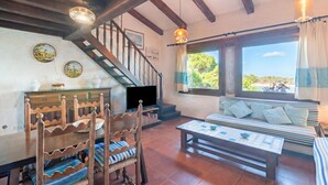 Un salon chaleureux avec un escalier en bois, une télévision, un canapé avec des coussins et une fenêtre donnant sur un beau paysage.