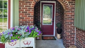 Une maison en briques avec une porte rouge, une boîte aux lettres blanche et un jardinier orné de fleurs violettes.