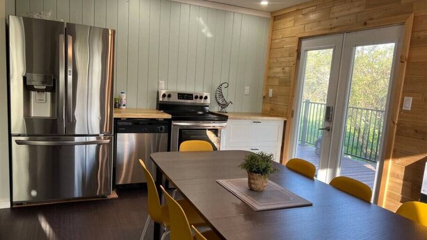 Une cuisine moderne équipée d’appareils électroménagers en acier inoxydable, une table à manger avec des chaises jaunes et une vue sur l’extérieur.