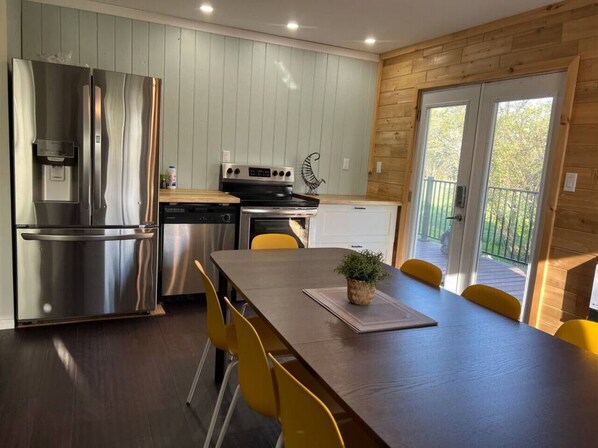 A modern kitchen with stainless steel appliances, a dining table with yellow chairs, and a view of the outdoors.