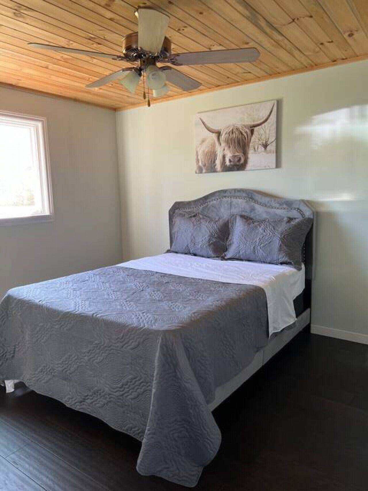 A bedroom with a bed, a ceiling fan, a window, and a wall-mounted picture of a bull.