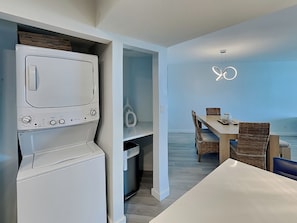 Une cuisine compacte dotée d’un four à micro-ondes et d’un four encastrés, un coin repas avec des chaises en osier et une vue sur la mer.