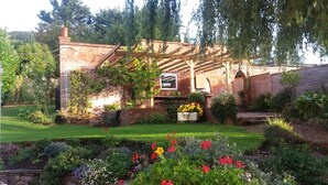 A garden with a brick wall, a pergola, and a variety of plants and flowers. - The Garden Studio, Woodcombe (Minehead)