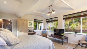A bedroom with a large bed, a TV, and a window with a view of greenery. - The Garden Studio, Woodcombe (Minehead)