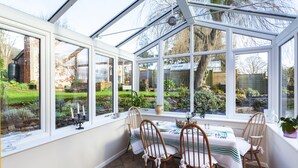 A conservatory with a table and chairs, large windows, and a garden view. - The Garden Studio, Woodcombe (Minehead)
