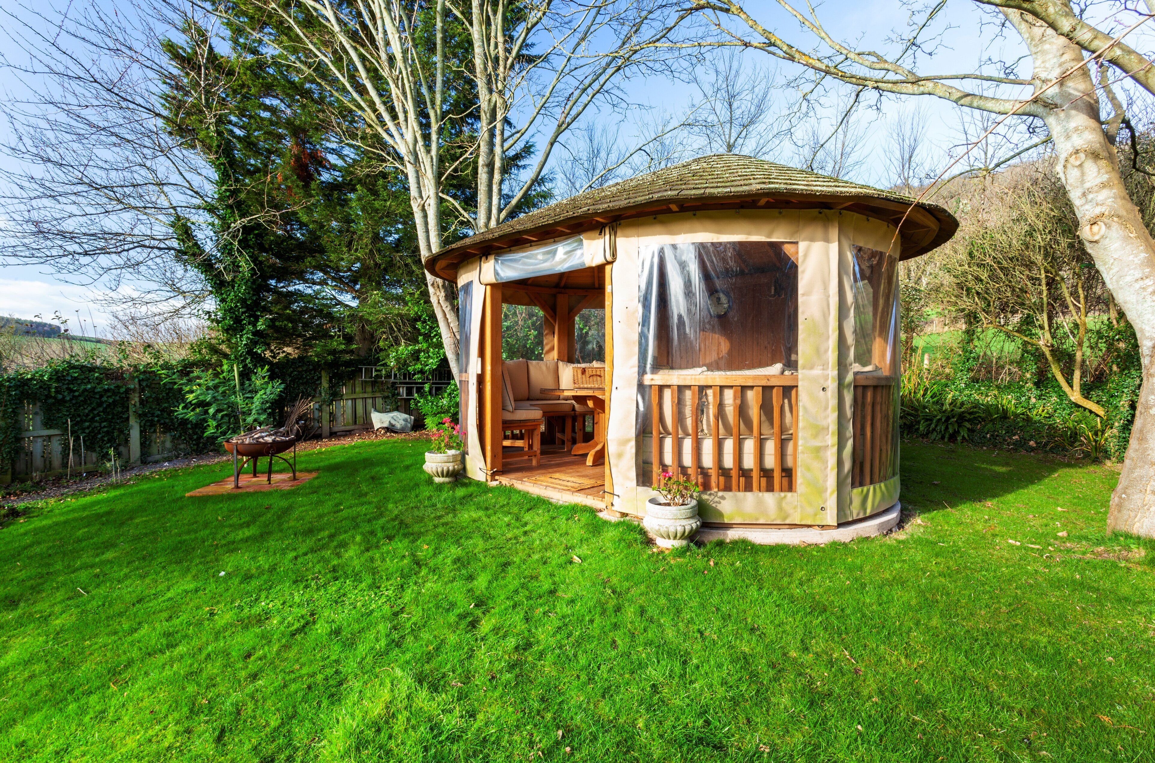 A wooden gazebo with a covered seating area, surrounded by a well-maintained lawn and trees.