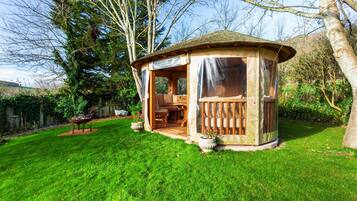 A wooden gazebo with a covered seating area, surrounded by a well-maintained lawn and trees.