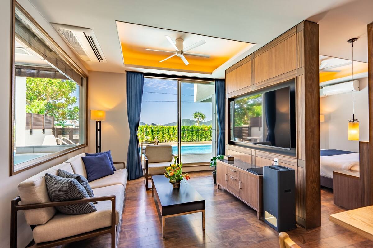Sala de estar moderna com sofá, mesa de centro, TV e vista para uma piscina.