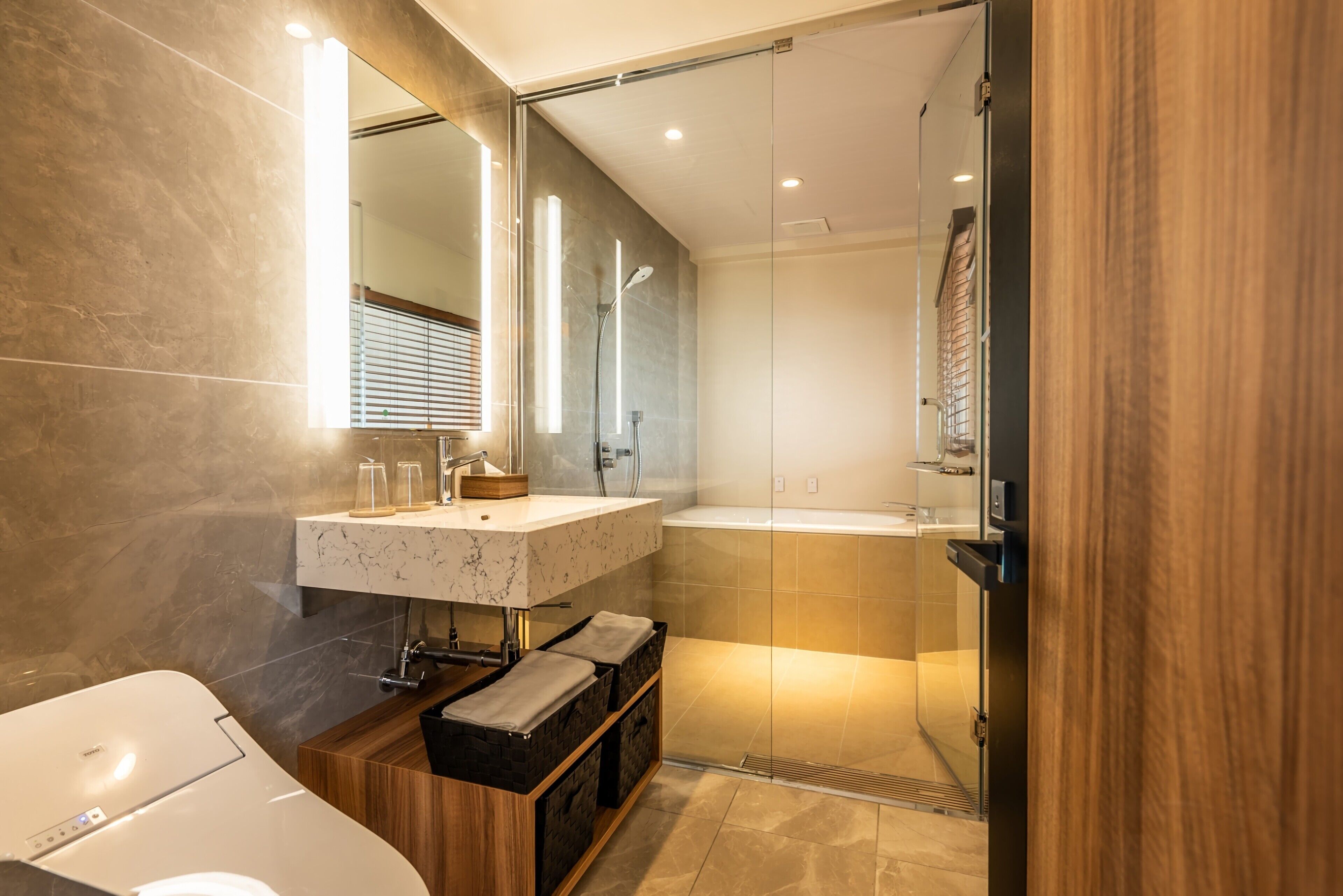 A modern bathroom with a marble sink, a glass shower enclosure, and a wooden vanity.