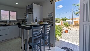 A kitchen with a dining area, a refrigerator, a microwave, and a sign indicating the ease of turning off lights and air conditioning. - Love and Peace Vacation Rental Aruba (Noord)