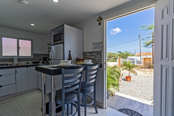 A kitchen with a dining area, a refrigerator, a microwave, and a sign indicating the ease of turning off lights and air conditioning.