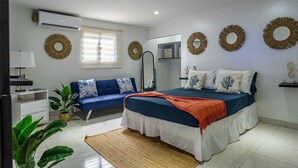 A bedroom with a bed, a sofa, a bedside table, a lamp, and a wall-mounted air conditioner. - Love and Peace Vacation Rental Aruba (Noord)