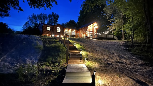 Une cabane en bois avec un escalier menant à une terrasse, entourée d’arbres et sous un ciel dégagé.