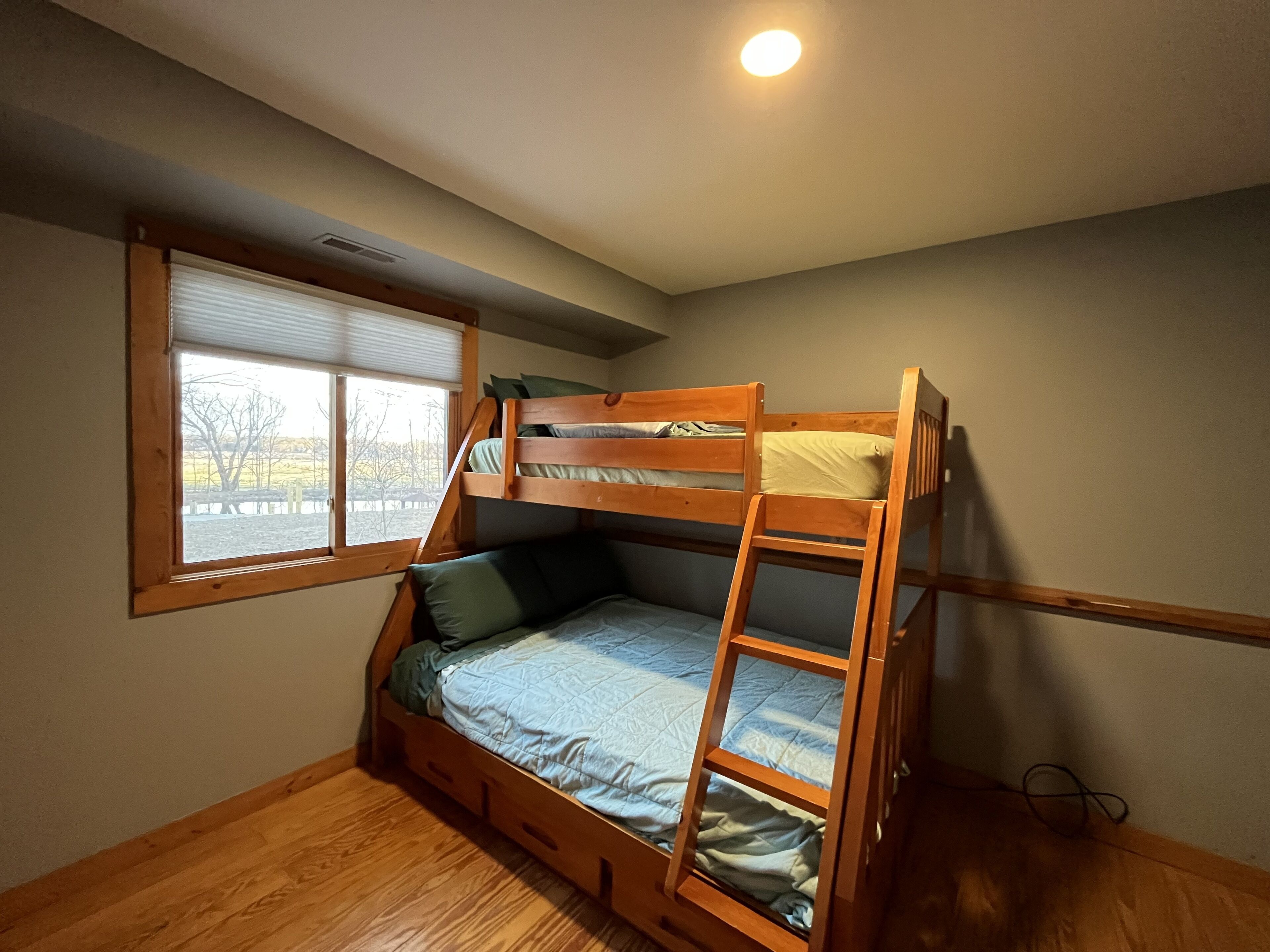 A bunk bed room with a window, wooden flooring, and a ceiling light.