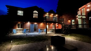Une cabane en rondins à deux étages, dotée d’un balcon, d’un espace extérieur aménagé pour s’asseoir et d’un escalier menant à l’étage supérieur.
