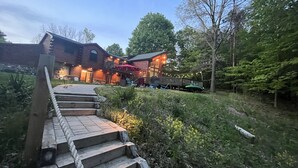 Une cabane en rondins avec un escalier en bois menant à une terrasse, le tout entouré d’une végétation luxuriante et d’arbres.