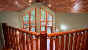 Un escalier en bois, doté d’une rampe, mène à un balcon avec de grandes fenêtres donnant sur une terrasse.