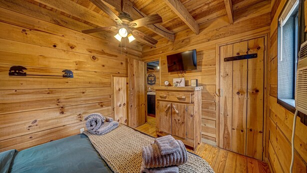 A wooden cabin room with a bed, a wooden cabinet, a mounted TV, and a ceiling fan.