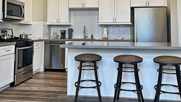 A modern kitchen with white cabinets, stainless steel appliances, and a central island with bar stools. - Upscale brand new beautiful 3bedroom, 2 story home! (Houston)