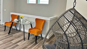 A dining area with a glass table, two orange chairs, a hanging chair, and two windows on the wall. - Upscale brand new beautiful 3bedroom, 2 story home! (Houston)