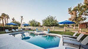 Une piscine entourée de chaises longues et de parasols, le tout délimité par une cour clôturée et agrémentée d’arbres.