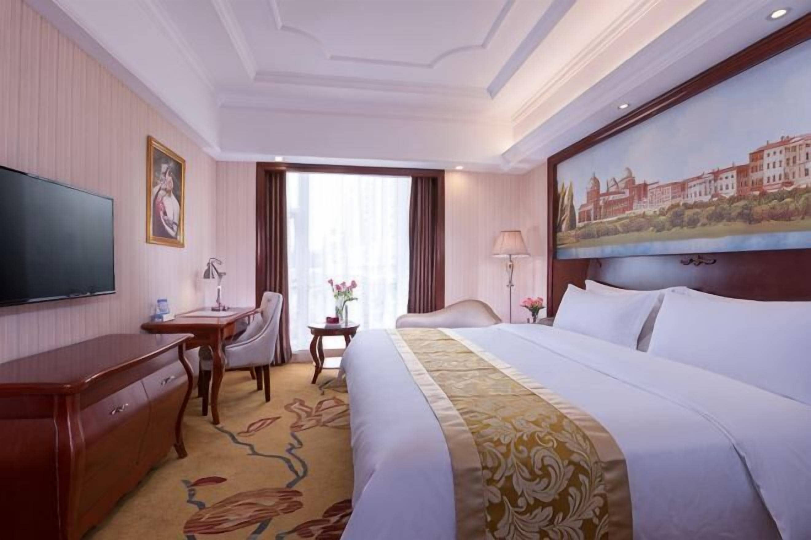 Une chambre d’hôtel avec un lit, un bureau, une télévision et un tableau au mur.
