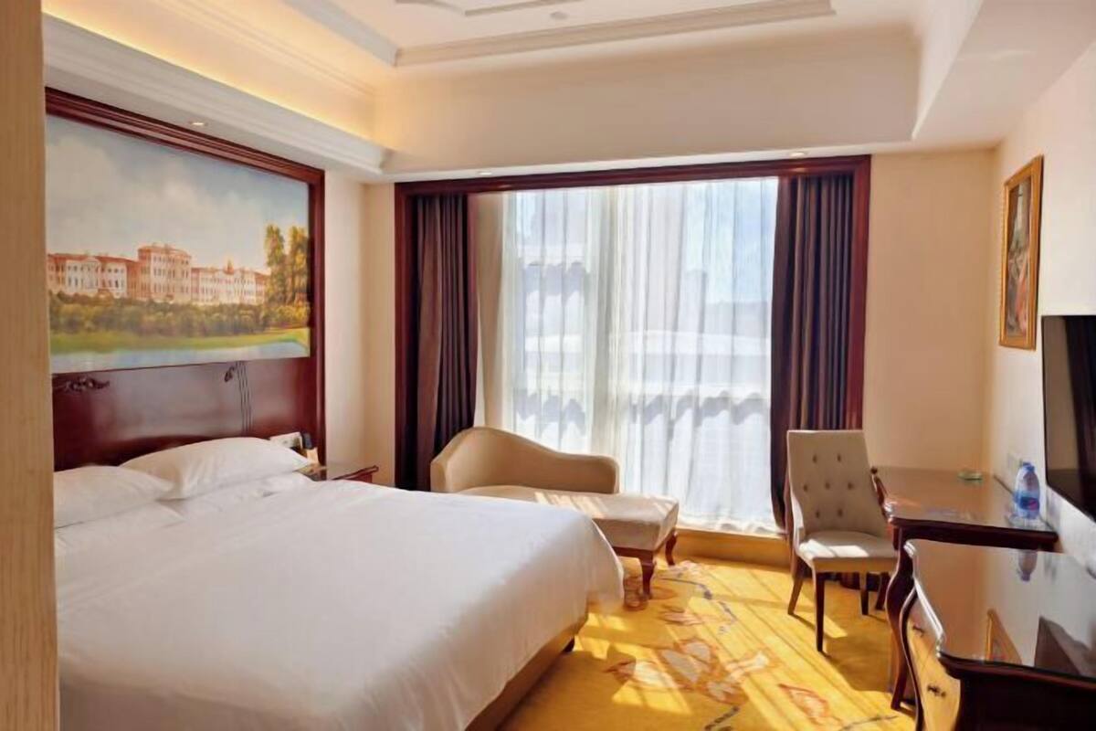 Ein Hotelzimmer mit einem großen Bett, einem Schreibtisch, einem Sessel und einem Bild an der Wand.
