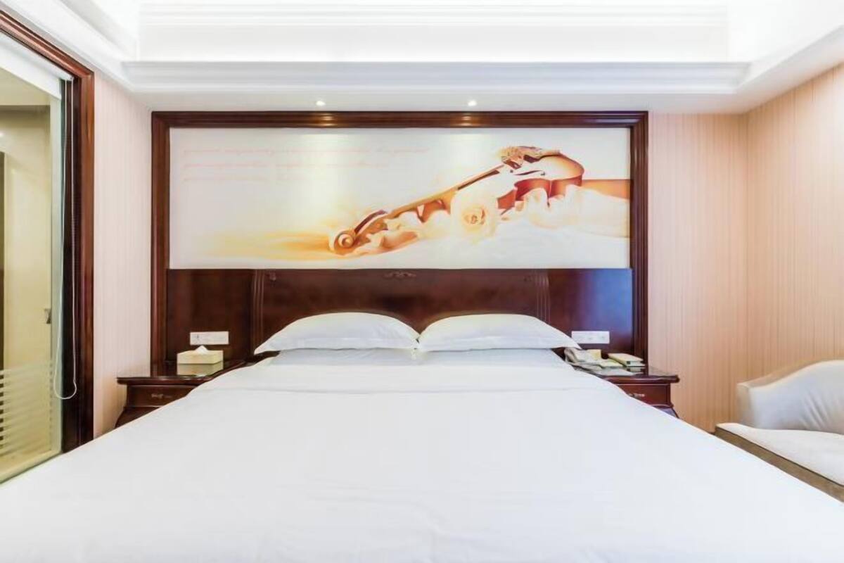 Ein Hotelzimmer mit einem großen Bett, einem Holz-Kopfteil, einem flachbildfernseher über dem Bett und einem Nachttisch mit einer Lampe.