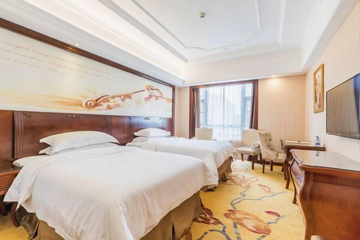 Ein Hotelzimmer mit zwei Betten, einem Schreibtisch, einem Stuhl und einem Fernseher.