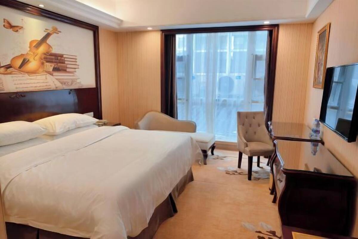 Ein Hotelzimmer mit einem Bett, einem Sessel, einem Schreibtisch, einem Fernseher und einem großen Fenster.