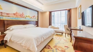 A hotel room with a large bed, a desk, a chair, a television, and a painting on the wall. - Vienna Hotel (Gaozhou Chengdong Passenger Station) (Gaozhou)
