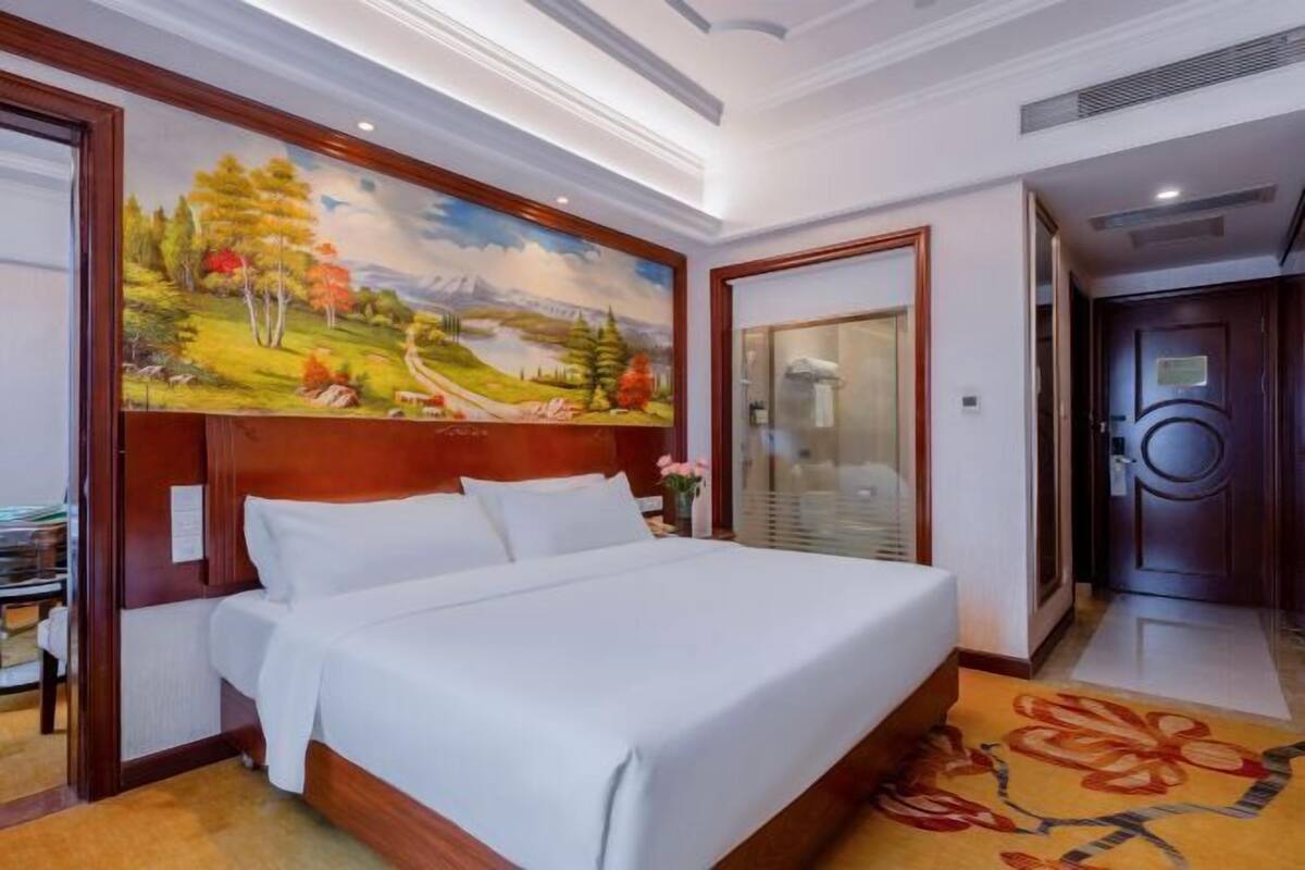 Ein Hotelzimmer mit einem großen Bett, einem Gemälde an der Wand und einem hölzernen Kopfteil.