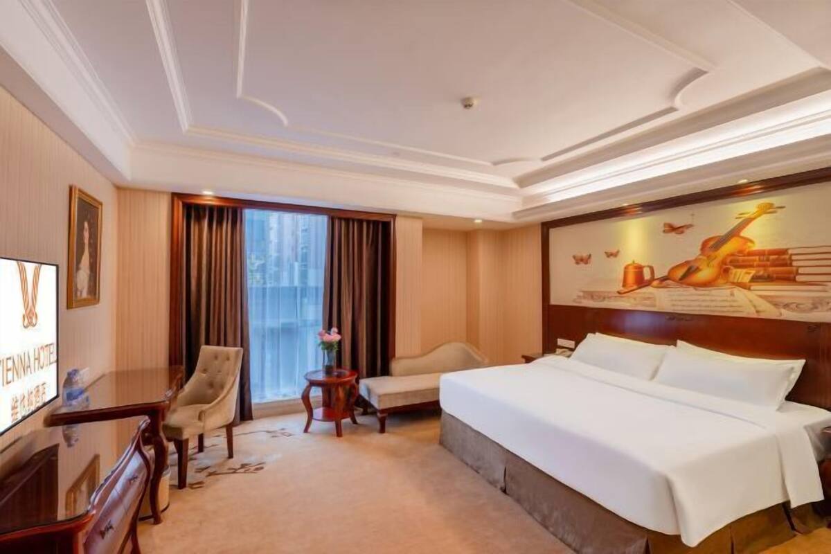 Ein Hotelzimmer mit einem großen Bett, einem Schreibtisch mit Stuhl, einem kleinen Beistelltisch und einem Fernseher.