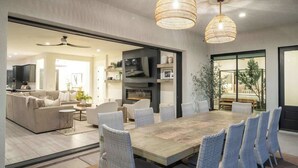 Un vaste espace de vie comprenant une grande table à manger, des chaises en osier et une cheminée.