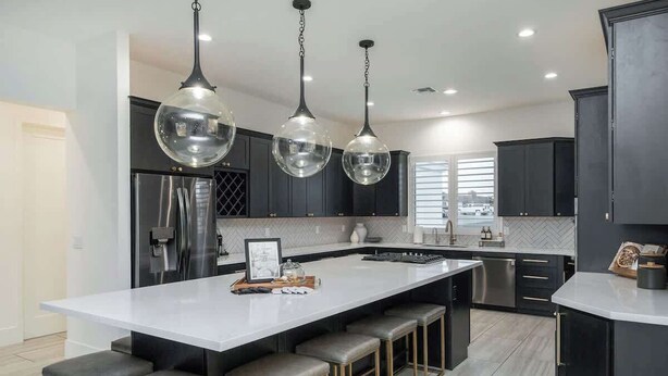 Une cuisine moderne dotée d’un grand îlot central, de luminaires suspendus, de meubles de couleur sombre et offrant une vue sur l’extérieur.