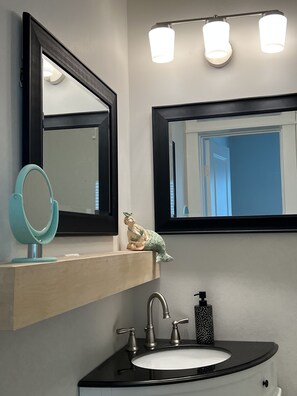 Bathroom features a large mirror, wall-mounted light fixture, and a black sink with a white basin.