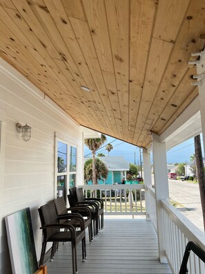 A covered porch with wooden beams, white railings, and black wicker chairs.