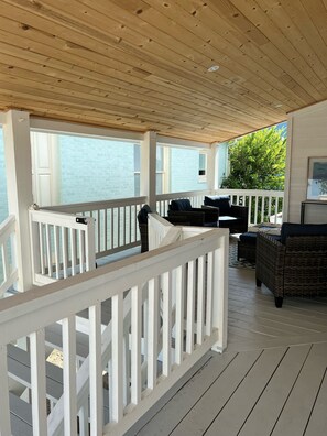 Eine überdachte Terrasse im Freien mit weißen Geländern, Korbmöbeln und Blick auf das Wasser.