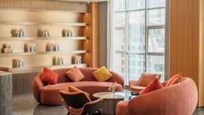 A modern lounge area with a red sofa, a round coffee table, and a seating area with a curved bench. Shelves with items are visible in the background. - Nujiang Hotel (Lushui)