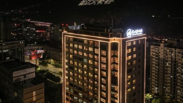 A high-rise building with illuminated windows and a sign at the top. - Nujiang Hotel (Lushui)