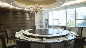 A round dining table with chairs, a chandelier, and a view of the city through large windows. - Nujiang Hotel (Lushui)