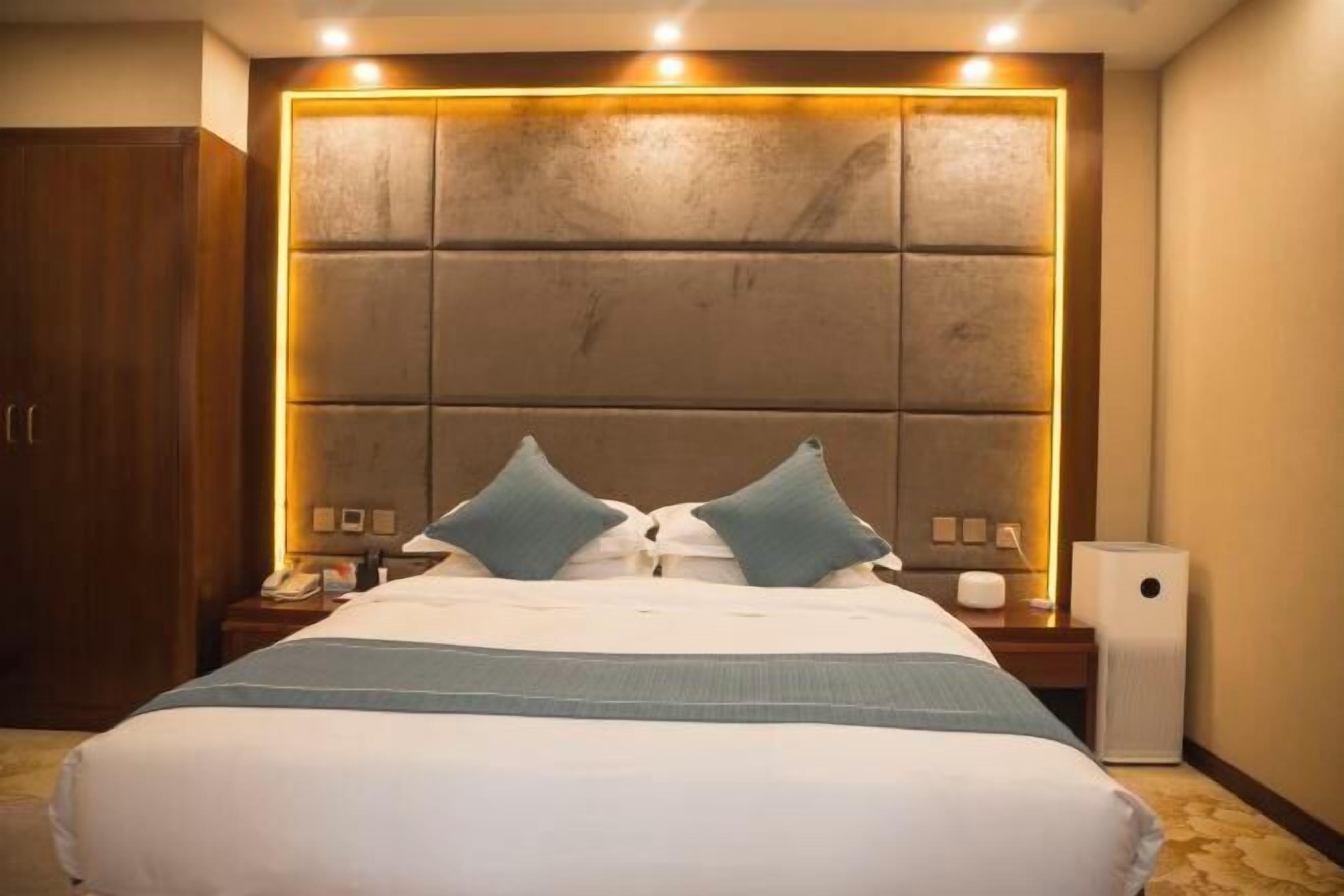 Quarto de hotel com cama grande, cabeceira de madeira, mesas de cabeceira com luminárias e telefone ao lado da cama.